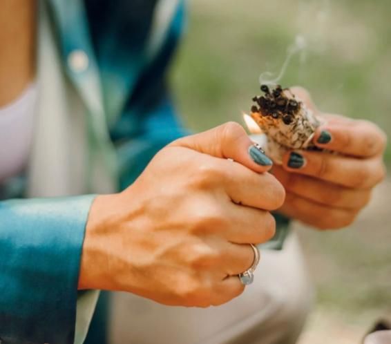 Hands lighting a bundle of white sage, with a thin line of smoke rising